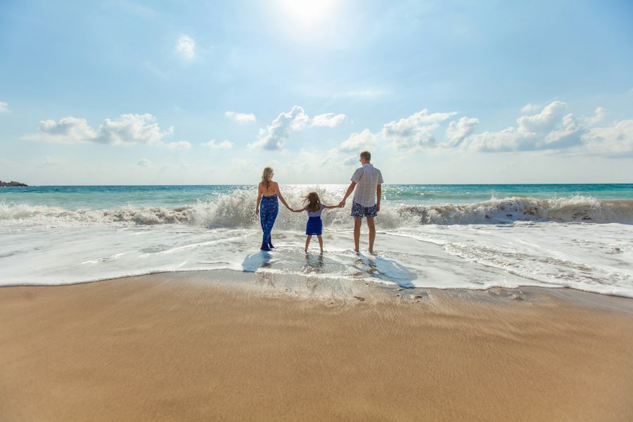 Família com uma criança de mãos dadas entrando no mar